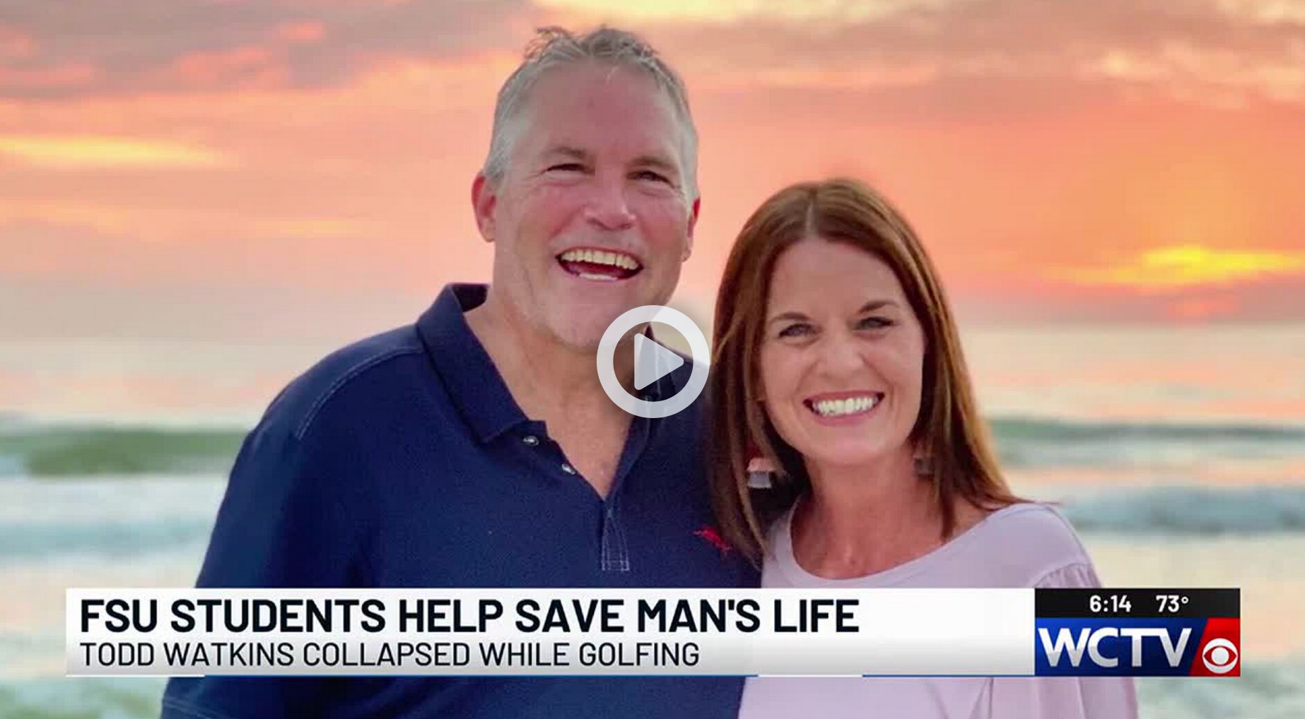 still picture of Todd Watkins and his wife posing in front of asunset. There is a play button superimposed over their faces.
