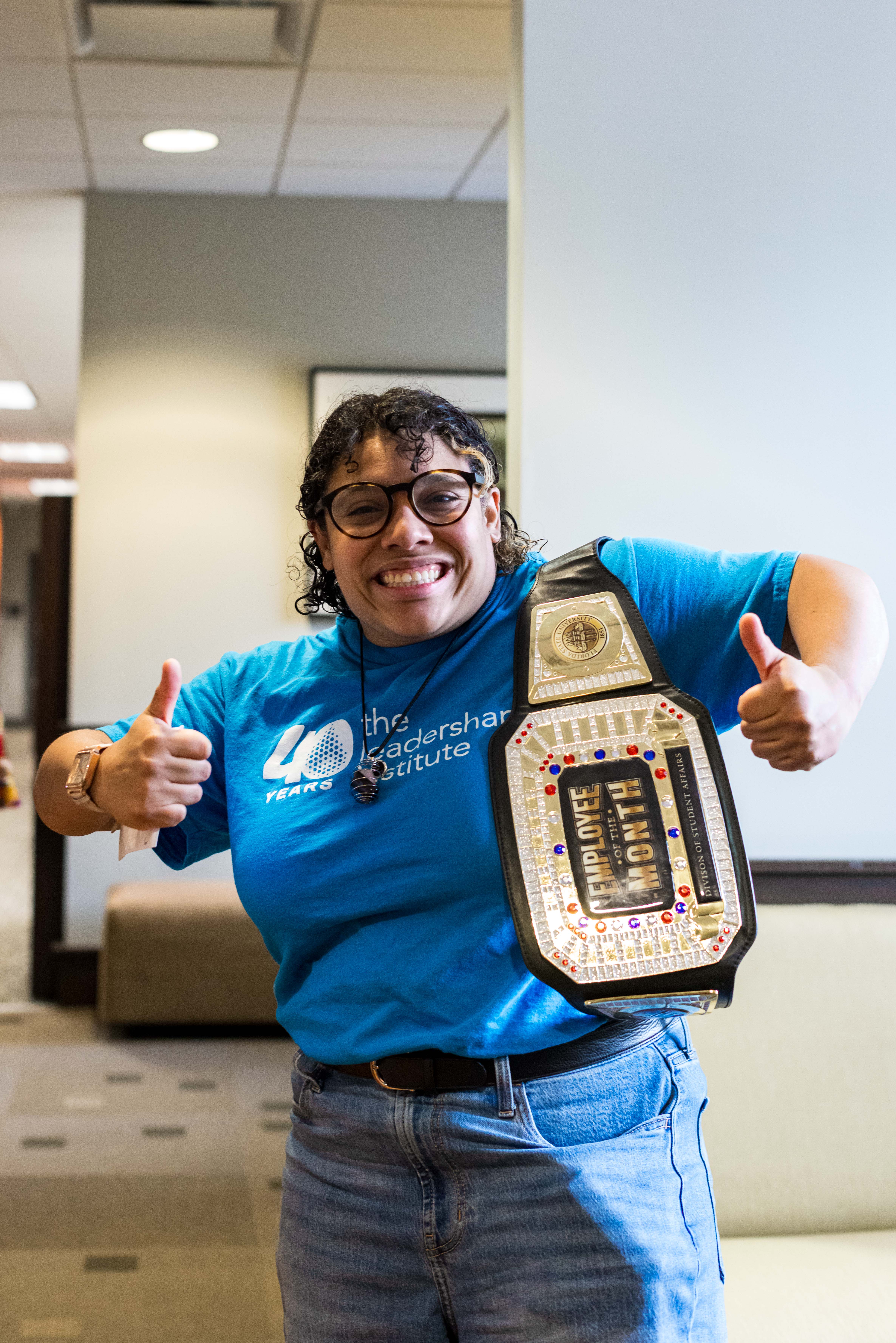Gen Ramirez smiling and giving thumbs up while holding the Employee of the Month belt