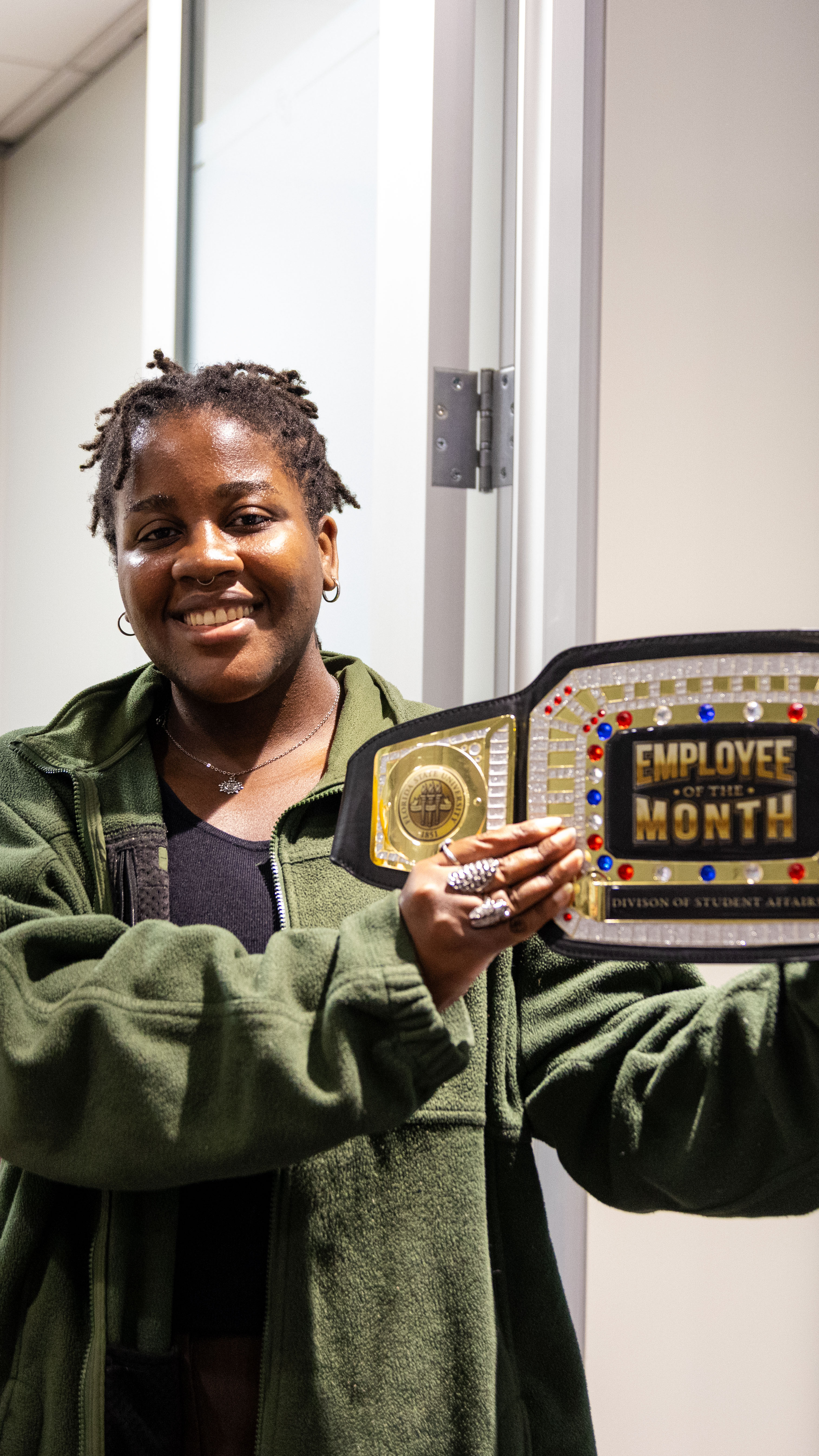 woman in green sweater holds the employee of the month belt